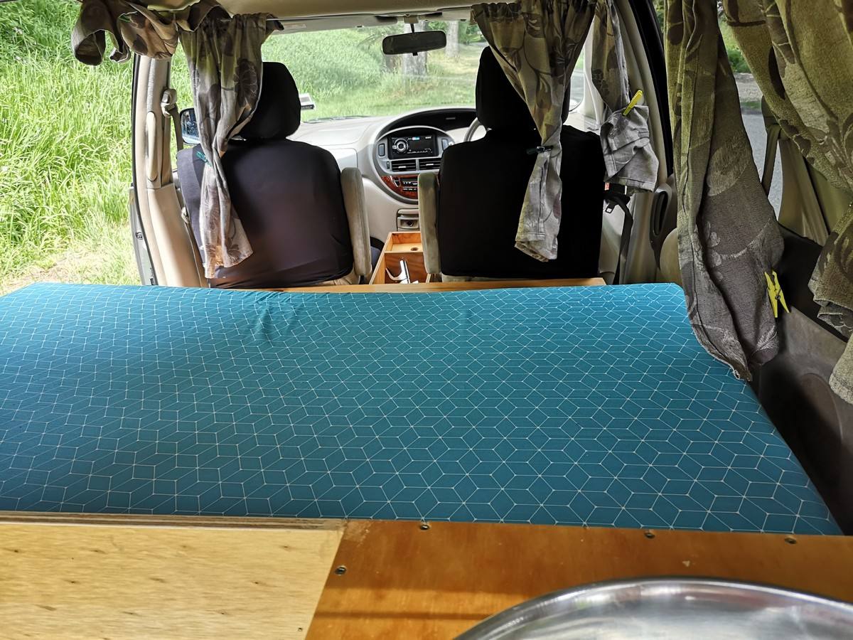 Inside the KBZ76 campervan, bed made up looking forward to the front seats, sink unit on the right