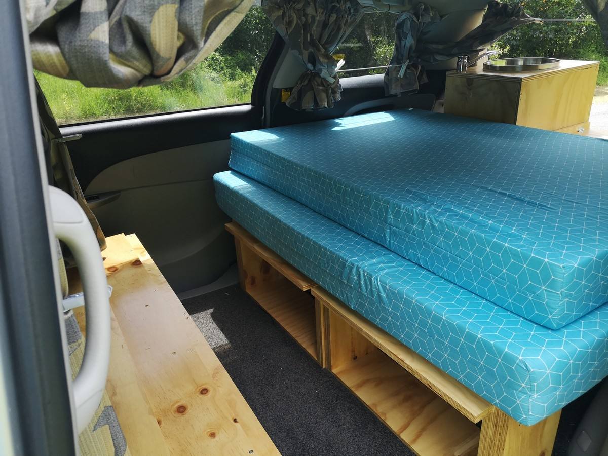 Side door open on the JTQ214 campervan, bed on its frame with storage space underneath