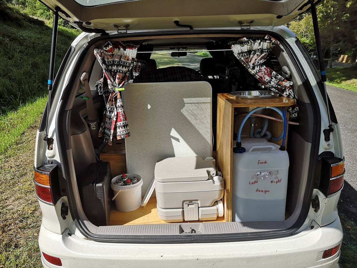 Tailgate open on the FQK81 campervan, showing the portable toilet, sink unit and fresh water container