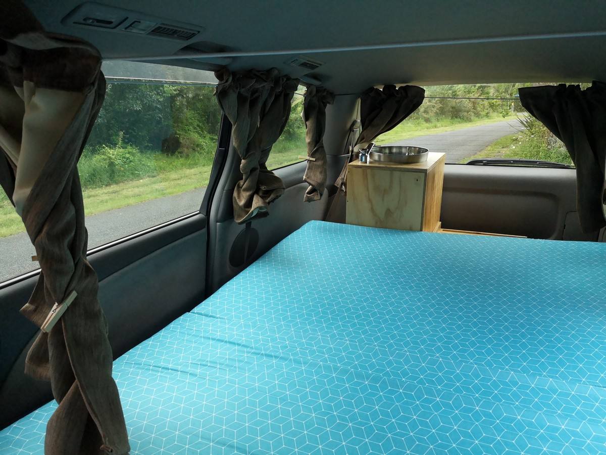 Inside the EZQ488 campervan with the curtains tied back, bed made up alongside the sink unit