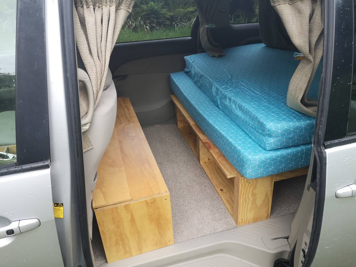 Side door open on the JNQ545 campervan, bed cushions on the timber base with the bench alongside