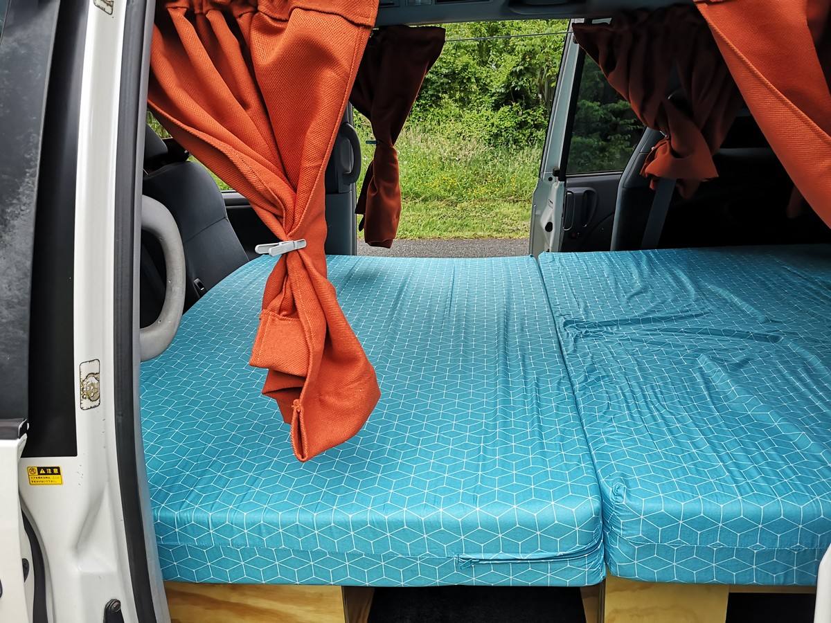 The HDP33 campervan's double bed made up across the van, orange curtains tied back