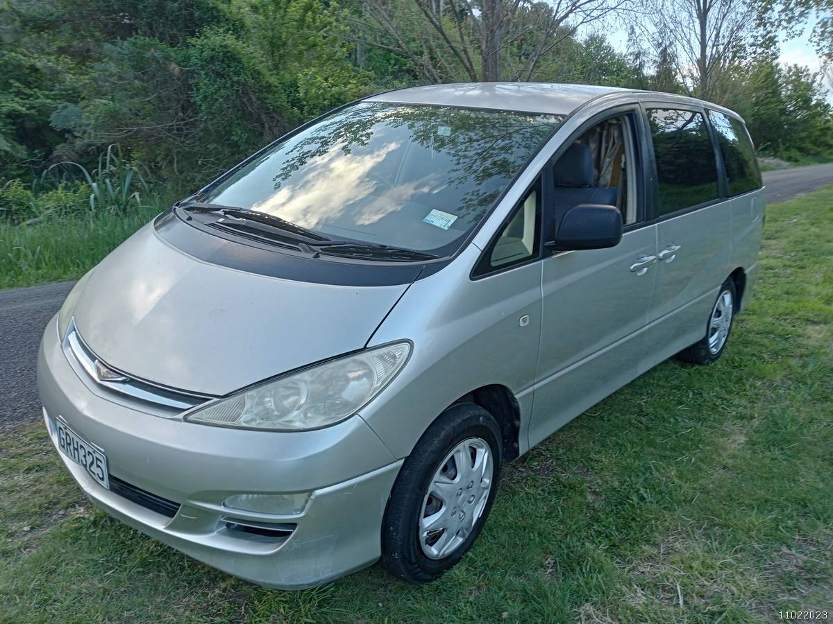 Front three-quarter view of the silver GRH325 Toyota Estima campervan on a country road