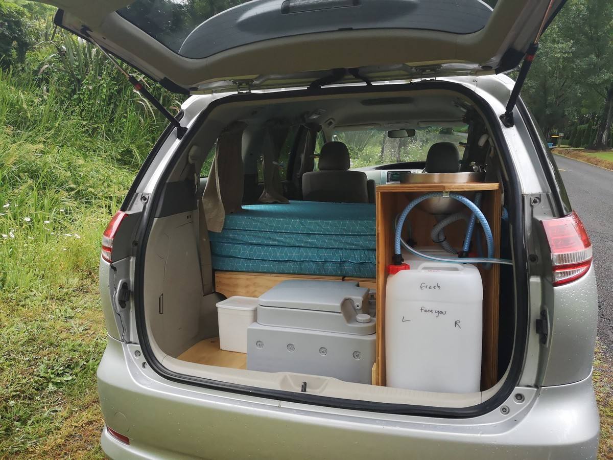 Tailgate open on the JNQ545 Toyota Estima campervan, bed, kitchen unit and water container packed inside