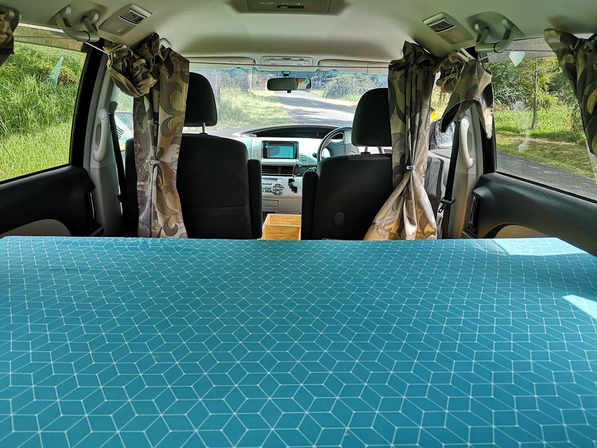 Inside the JTQ214 campervan, full-width bed made up looking forward to the front seats