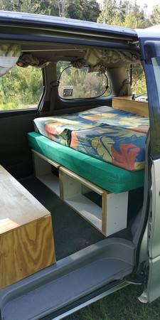 Side door open on the GBB26 campervan, bed made up over the open storage shelves with a step below