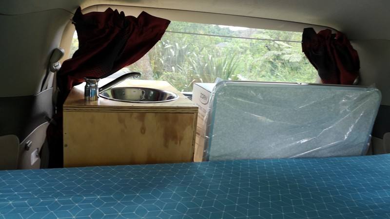 Inside the HMC107 campervan, stainless sink in the plywood bench with the mattress stood on edge beside it