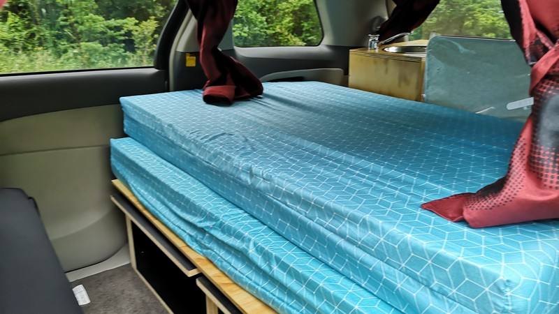 The HMC107 campervan's bed made up, looking along it towards the sink unit