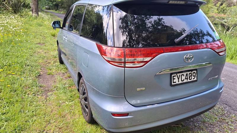 Rear three-quarter view of the blue 2007 Toyota Estima campervan EYC409 parked on grass