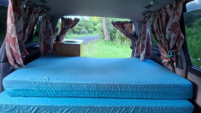Inside the ERT416 campervan, double bed made up looking out through the open tailgate