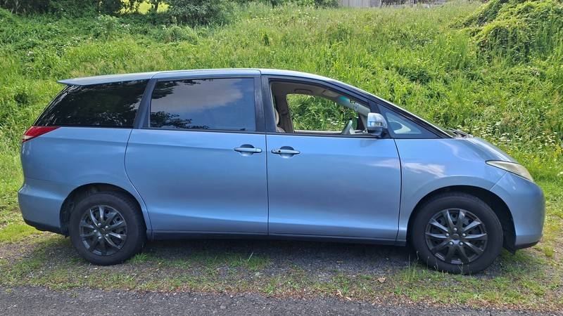 Side view of the blue 2007 Toyota Estima campervan EYC409 parked on a grass verge