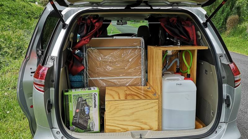 Tailgate open on the HMC107 campervan, packed with camping chairs, table, water container and the kitchen unit