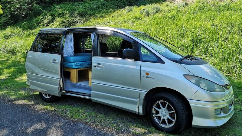 Side door open on the silver FYC899 Toyota Estima campervan, bed and storage visible inside