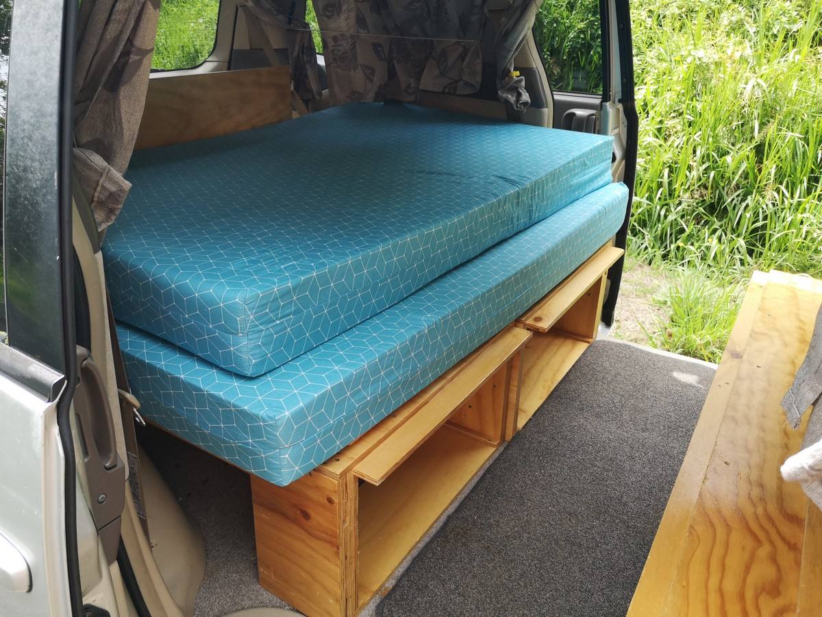 Side door open on the KBZ76 campervan, bed cushions on the plywood base with storage underneath