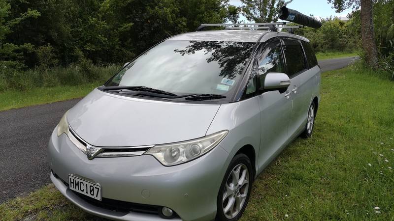 Front three-quarter view of the silver HMC107 Toyota Estima campervan with its roof rack and awning