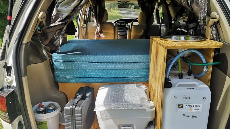 Inside the GQG541 campervan, bed cushion on its base beside the kitchen unit and the water container