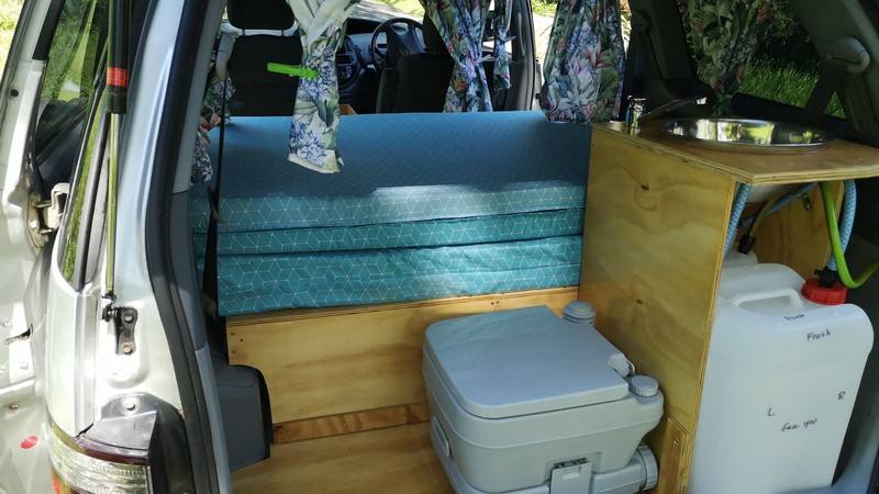 Inside the FYC899 campervan, bed cushions stacked beside the portable toilet and the sink unit