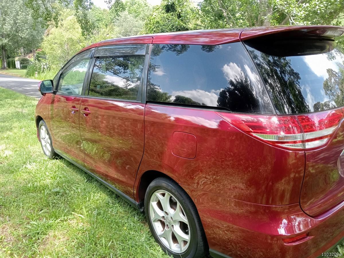 Rear three-quarter view of the red 2006 Toyota Estima campervan JAK653 parked on grass