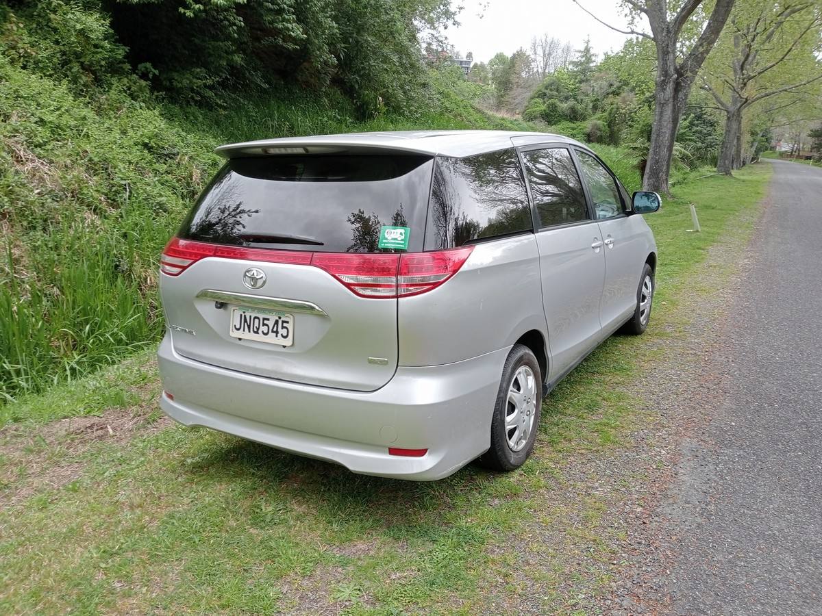 Rear three-quarter view of the silver 2006 Toyota Estima campervan JNQ545 on a country road