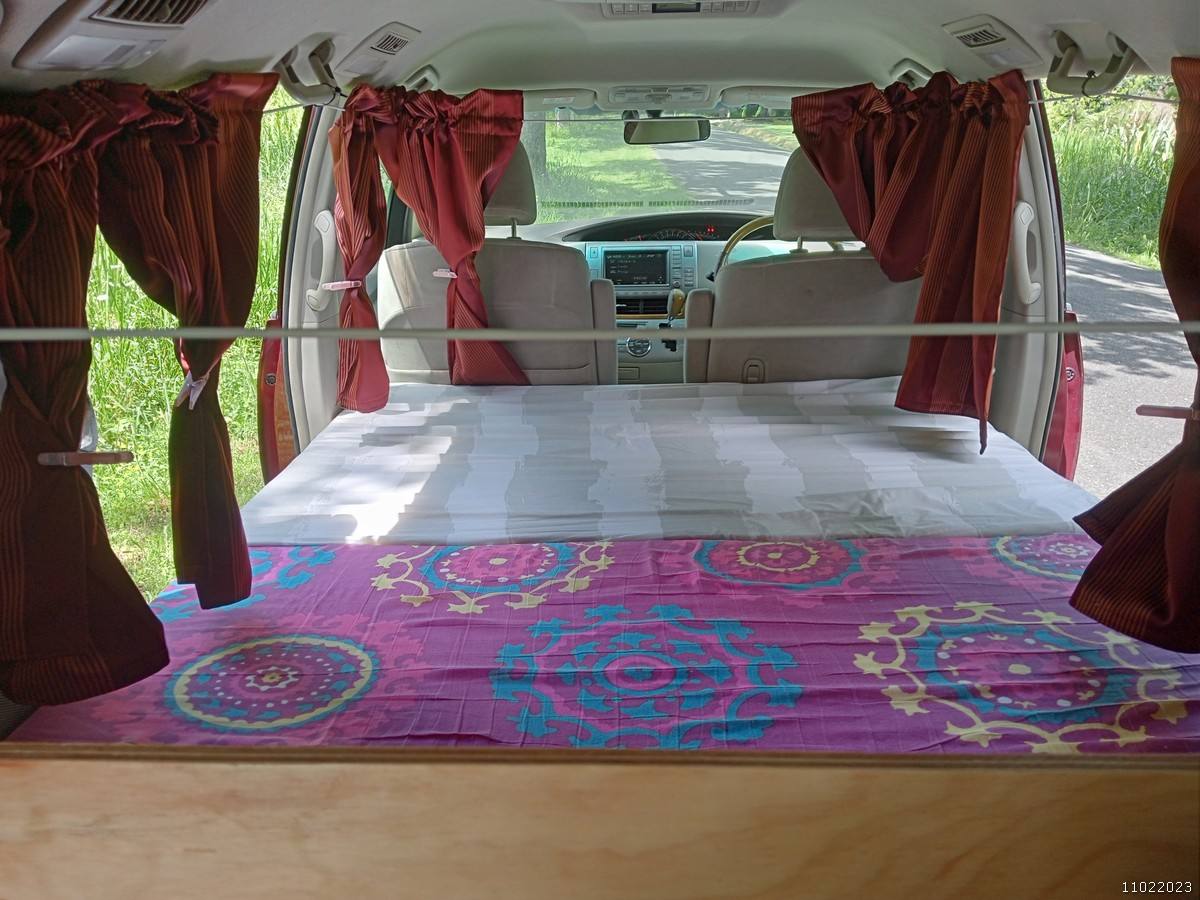 Inside the JAK653 campervan looking forward over the made-up bed to the front seats, red curtains tied back
