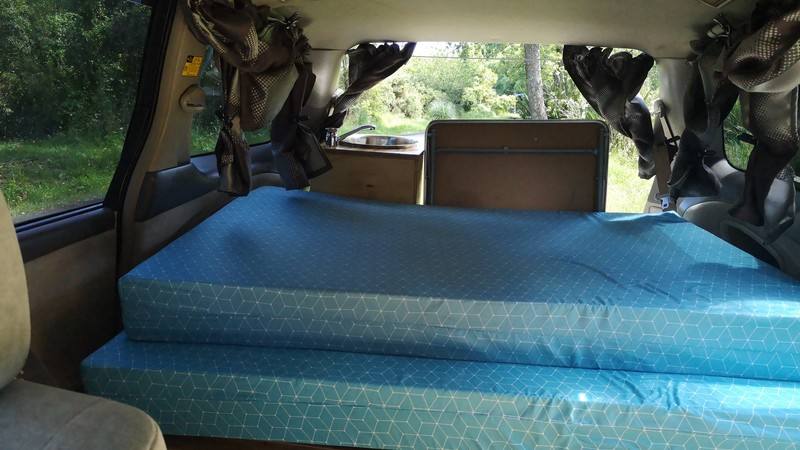 Inside the GQG541 campervan looking across the made-up bed, curtains tied back at the windows