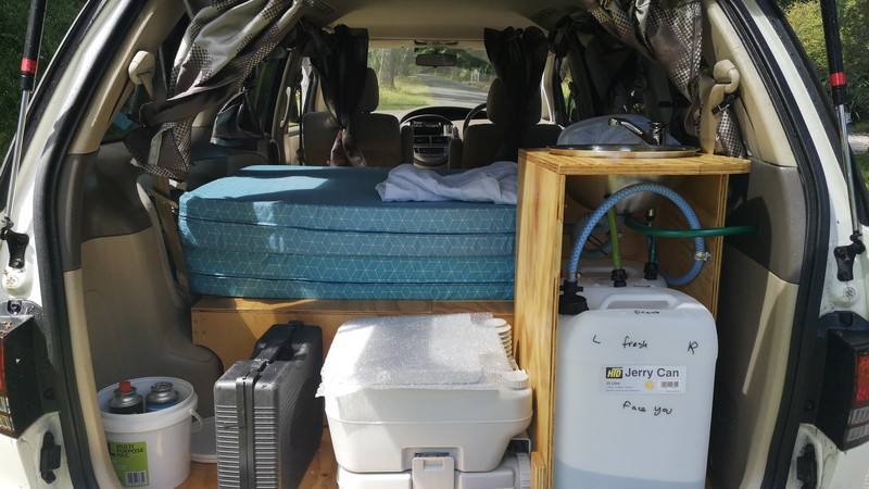 Tailgate open on the GQG541 campervan, showing the bed, kitchen unit, portable toilet and water container