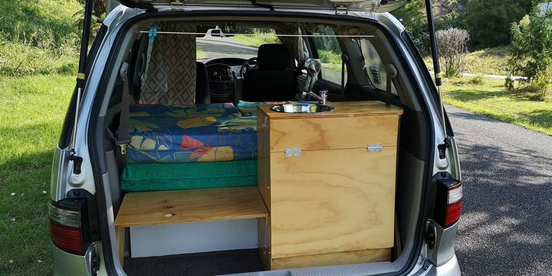 Tailgate open on the GBB26 campervan, showing the plywood kitchen unit with stainless sink beside the bed
