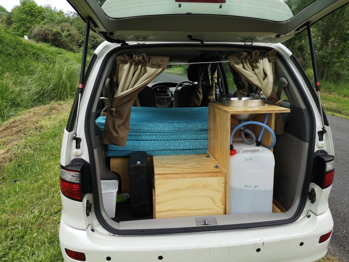 Tailgate open on the EZQ488 campervan, showing the bed, kitchen unit and fresh water container