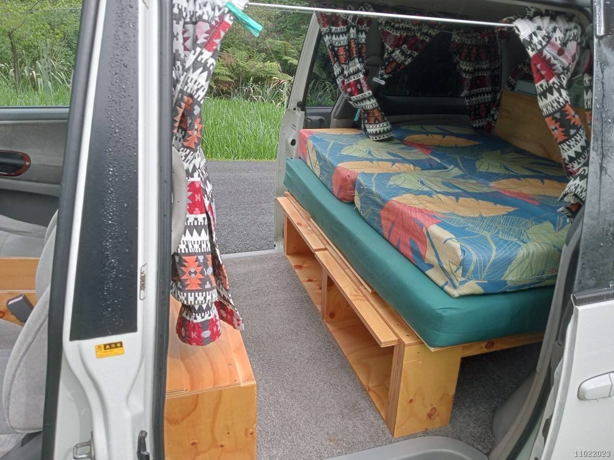 Side door open on the FQK81 campervan, bed on its timber frame with the bench alongside
