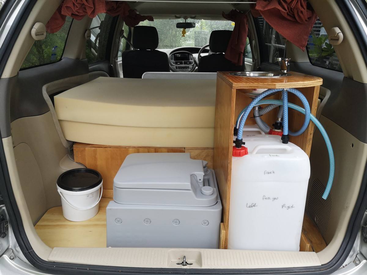 Tailgate open on the GRH325 campervan, showing the bed, portable toilet, sink unit and water container