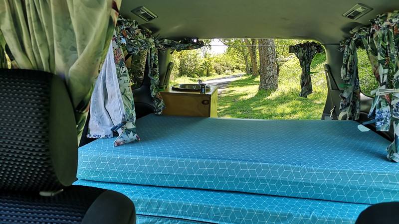 Inside the FYC899 campervan, bed made up looking out through the open tailgate to the trees