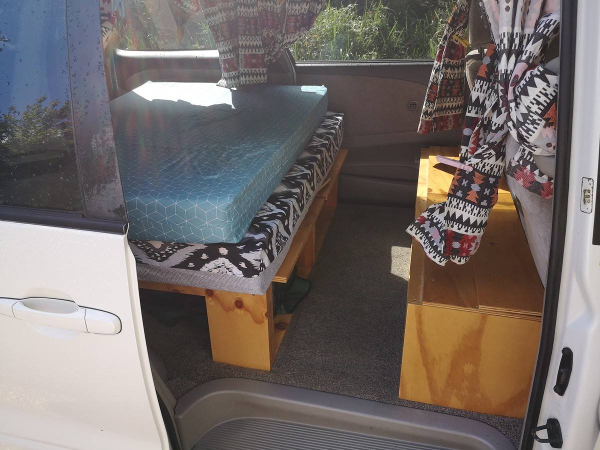 Side door open on the FQK81 campervan, bed made up on its plywood base with storage boxes alongside