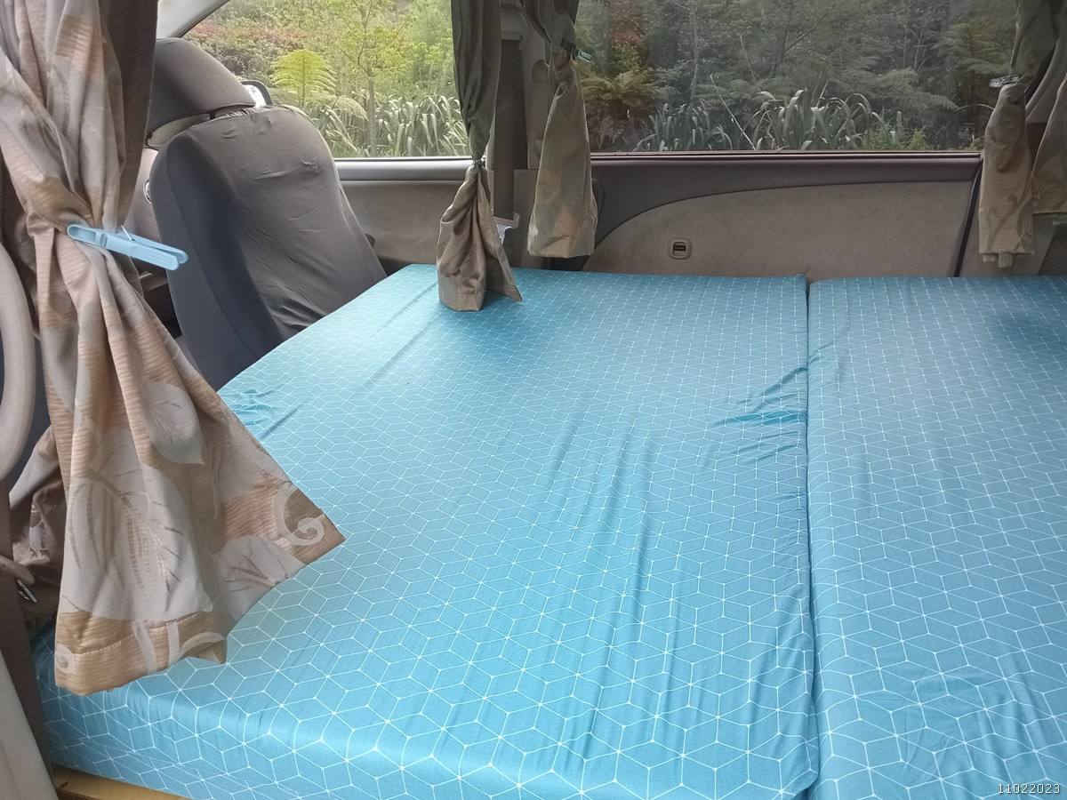 The GRH325 campervan's double bed made up across the van, curtains tied back