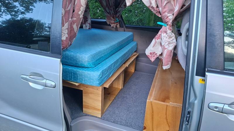 Side door open on the ERT416 campervan, bed cushion on its plywood base with storage underneath