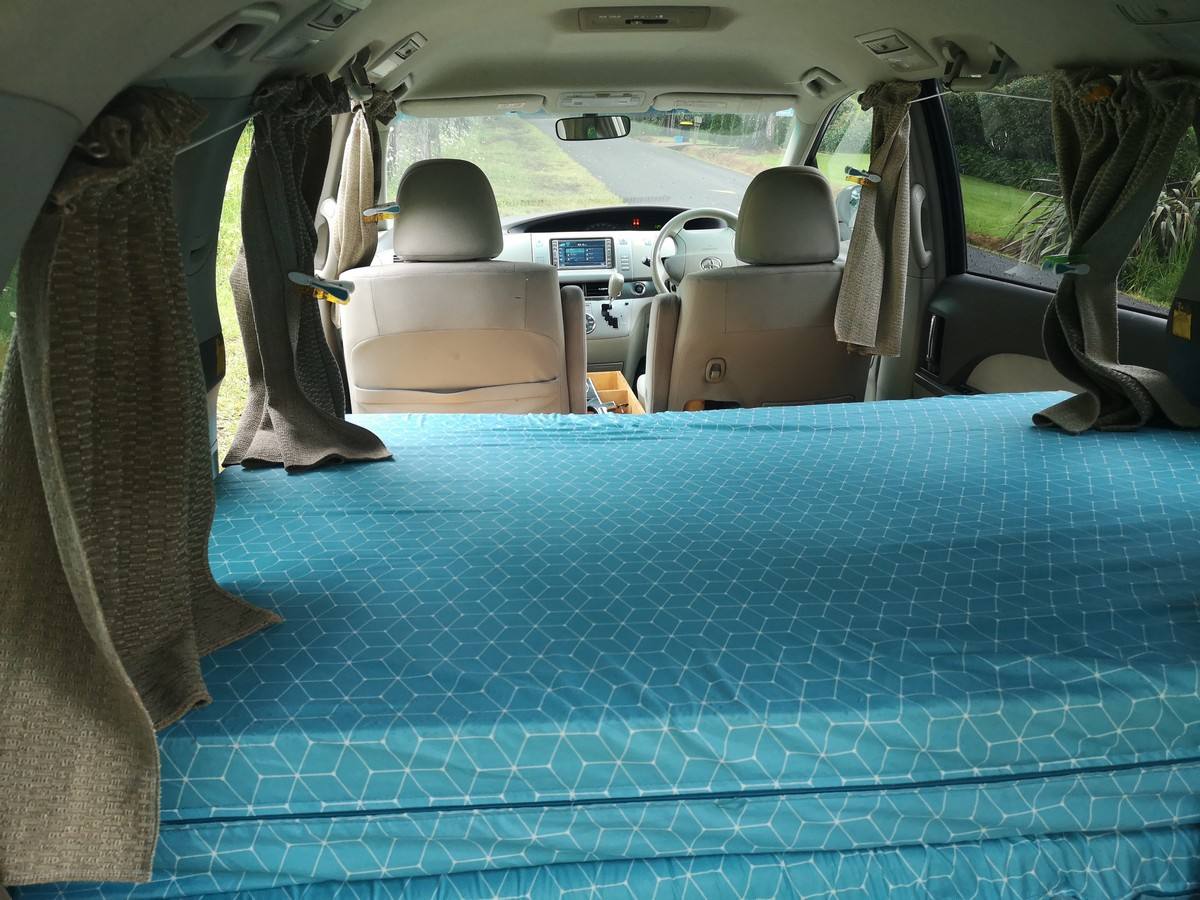 Inside the JNQ545 campervan, full-width bed made up looking forward to the front seats