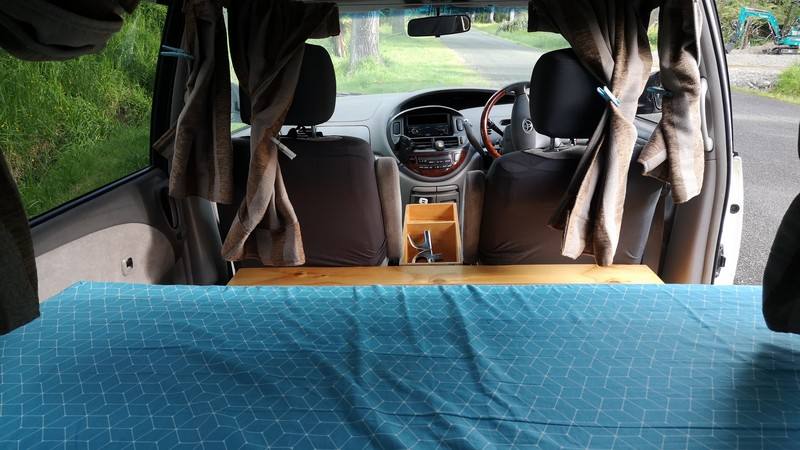 Inside the campervan looking forward over the bed to the front seats and dashboard, curtains tied back