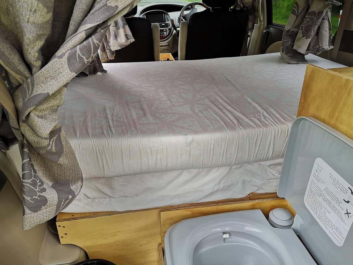 Inside the KZR927 campervan, made-up bed beside the portable toilet