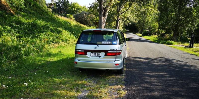 Back of the silver Toyota Estima campervan with registration GBB26, parked under trees