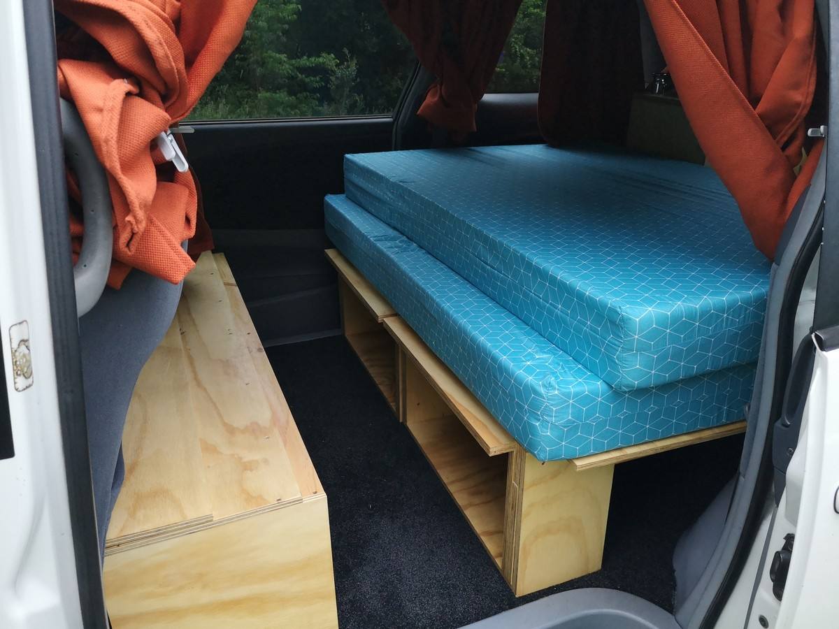 Side door open on the HDP33 campervan, bed on its plywood base above the storage, bench seat alongside