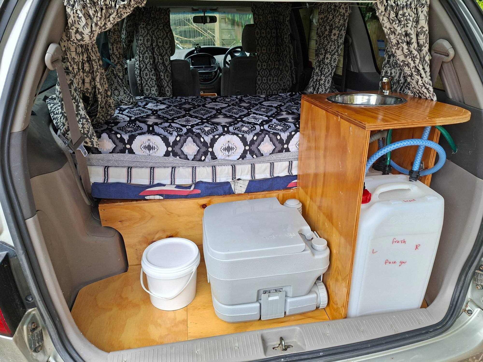 Tailgate open on the FPS382 campervan, showing the bed, sink unit, portable toilet and water container