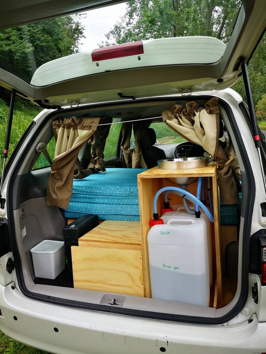 Tailgate open on the EZQ488 campervan, showing the bed, kitchen unit with sink and the water containers