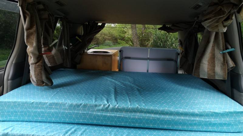 Inside the FAC789 Toyota Estima campervan, looking over the made-up double bed to the sink unit and the rear seats