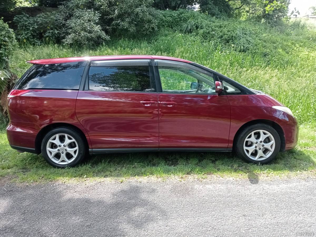 Side view of the red 2006 Toyota Estima campervan JAK653 on a country road