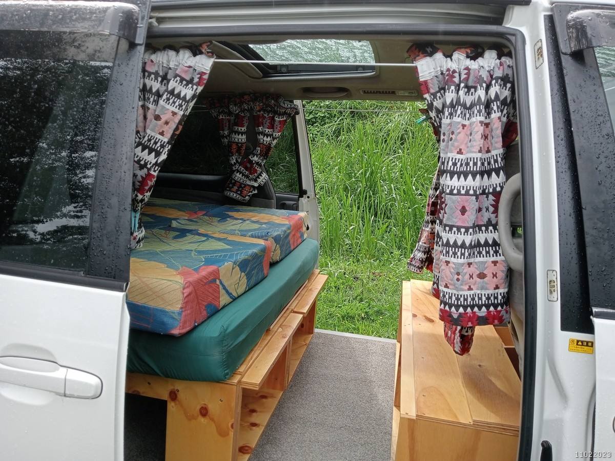 Inside the FQK81 campervan through the open side door, bed made up and the sunroof above