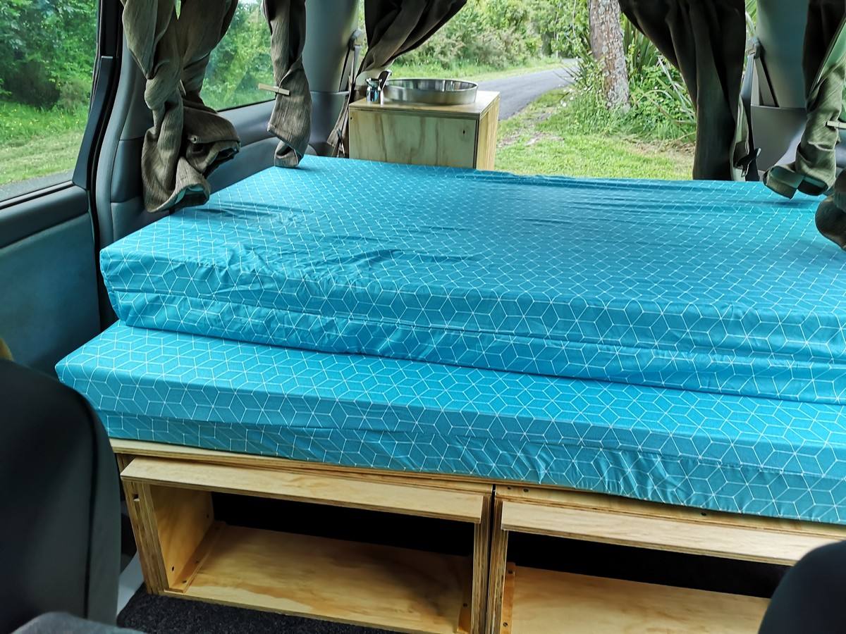Inside the EZQ488 campervan, double bed made up over the open storage shelves