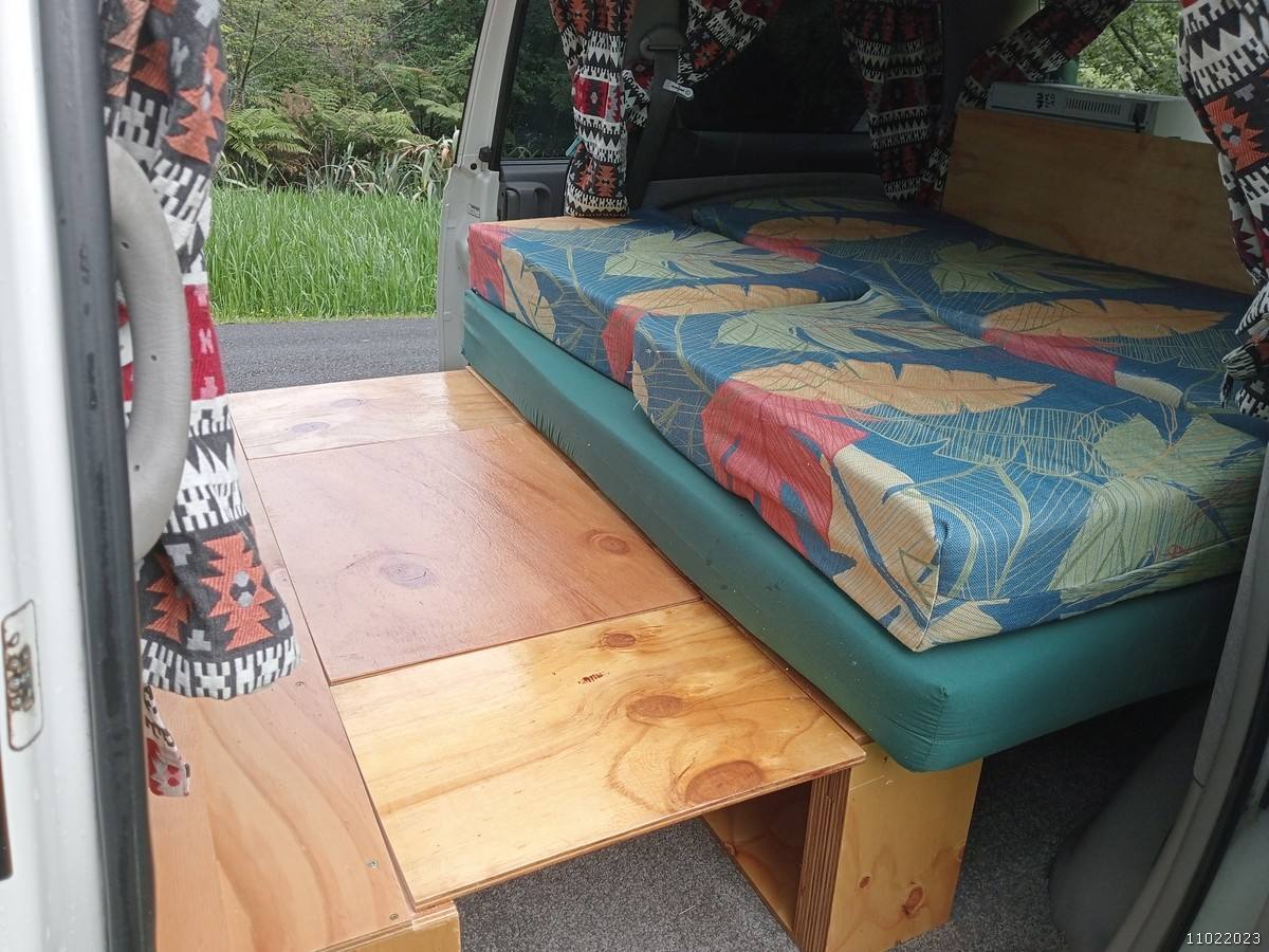 Inside the FQK81 campervan, bed cushion on its timber base with the plywood table folded out
