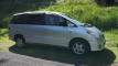 Silver 2000 Toyota Estima self-contained campervan for sale, side view parked on grass below a bush bank