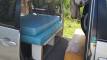 Side door open on the silver Toyota Estima campervan, bed made up over the storage shelves, step board alongside