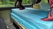 The HMC107 campervan's bed made up, looking along it towards the sink unit