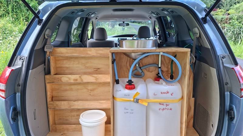 Tailgate open on the EYC409 campervan, showing the plywood shelving, sink unit and two water containers